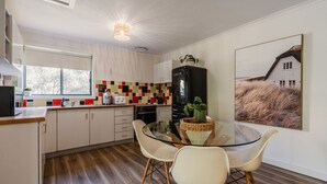 Una cocina moderna con mesa de comedor de vidrio, armarios blancos y un respuesto colorido.