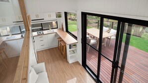 Una cocina moderna con armarios blancos y encimera de madera, que da a una puerta corrediza de cristal hacia una terraza exterior con mesa y sillas.