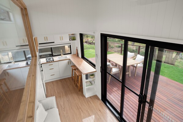 A modern kitchen with white cabinets and a wooden countertop, leading to a sliding glass door to an outdoor deck with a table and chairs.
