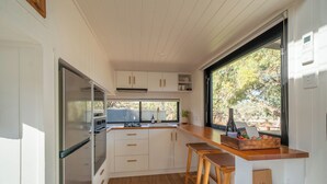 Cocina compacta con armarios blancos, encimera de madera y ventana con vistas al exterior.