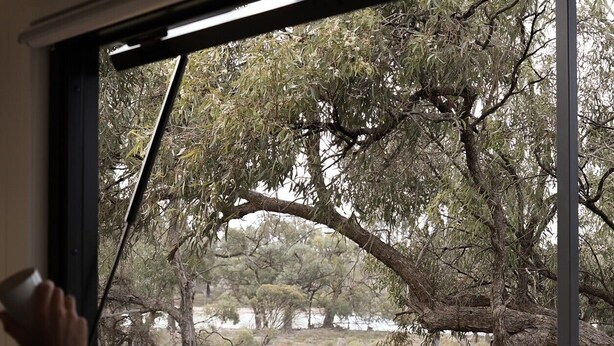 Un comedor con una mesa y sillas, una ventana que da a un paisaje natural con árboles y una cerca.