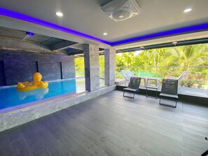 An indoor swimming pool with a yellow inflatable duck, lounge chairs, and a view of greenery outside. - Happy Hotel Ao Nang Krabi (Krabi)