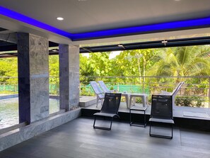 A modern indoor pool area with marble columns, lounge chairs, and a view of lush greenery. - Happy Hotel Ao Nang Krabi (Krabi)