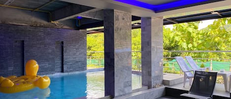 A modern indoor pool with a yellow inflatable float, marble walls, and a balcony with lounge chairs.