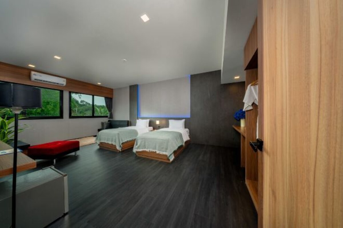 A modern hotel room with two beds, a desk, a TV, and a large window.