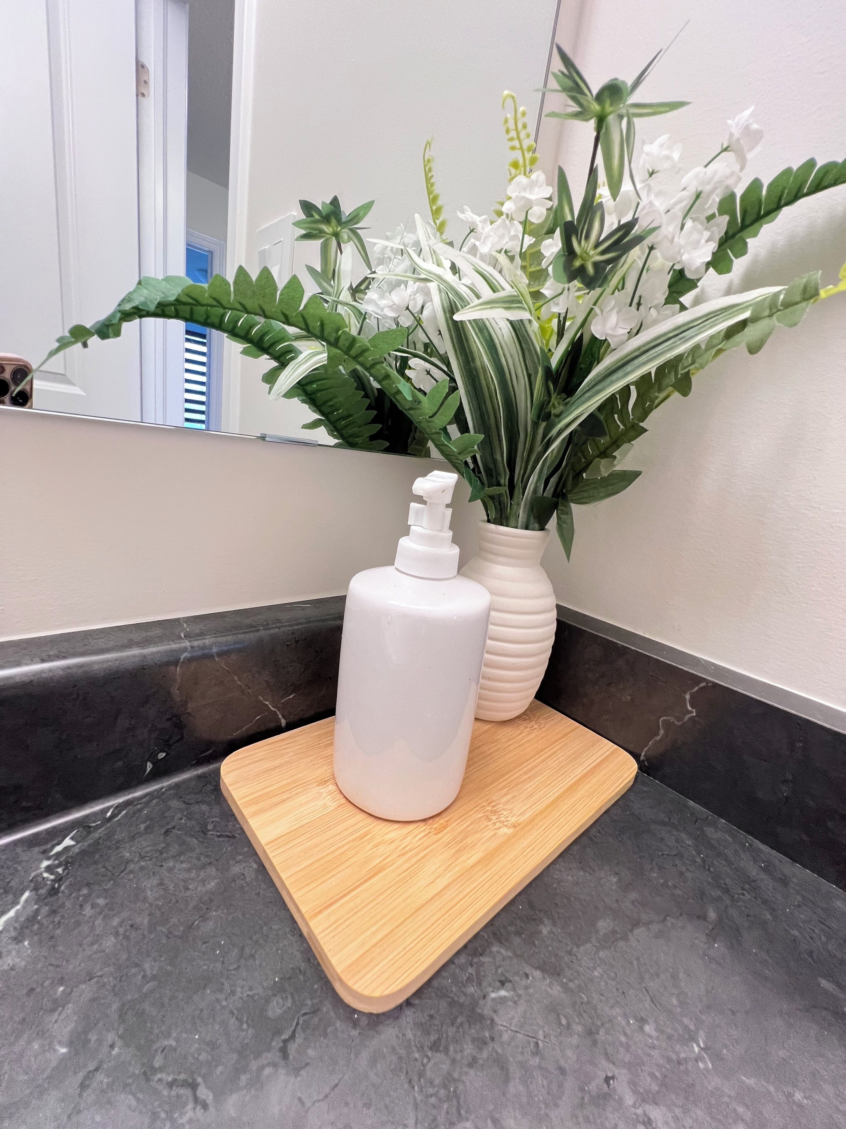 A bathroom with a marble countertop, a white bottle, and a vase with flowers.