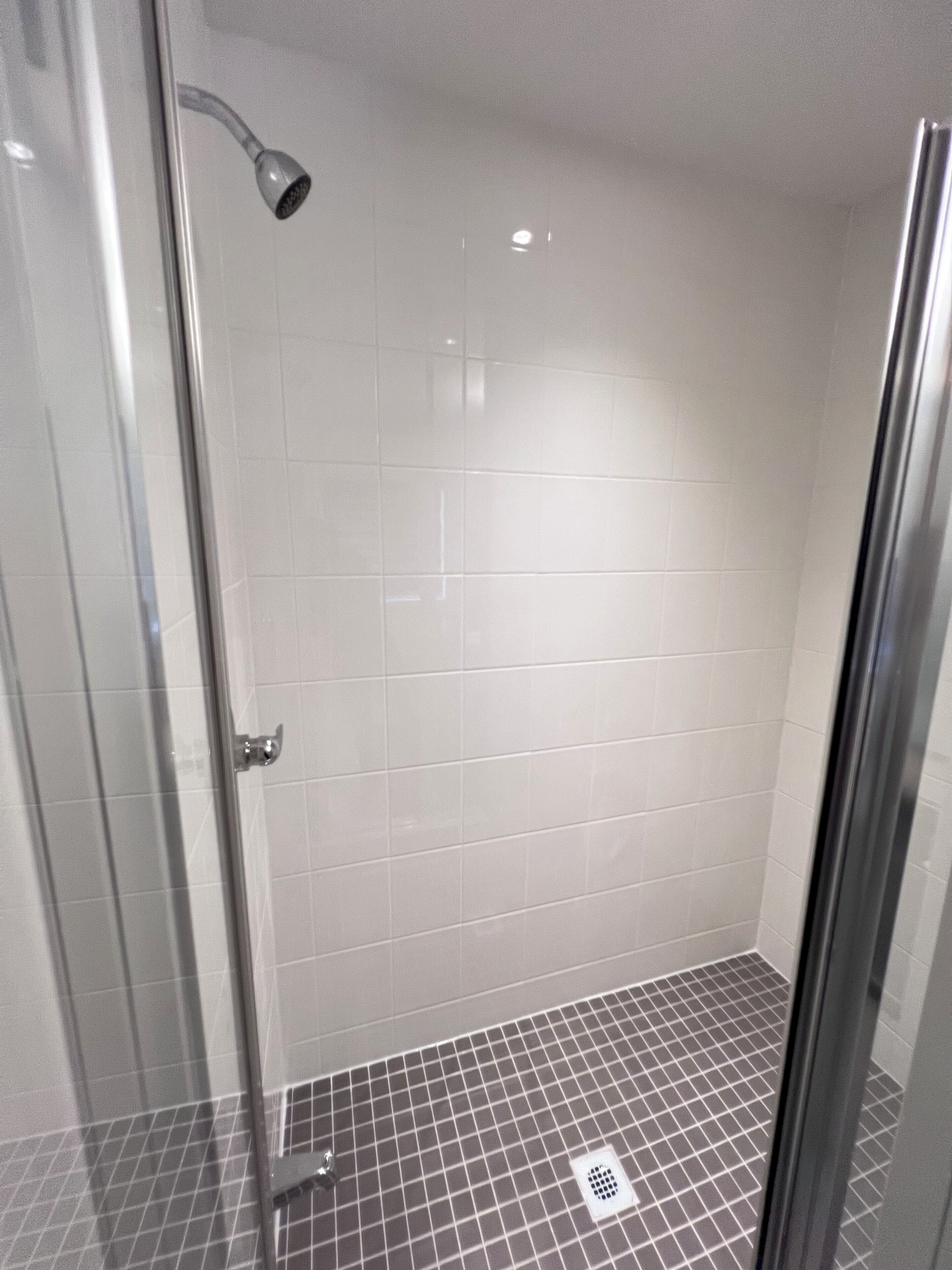 Eine begehbare Dusche mit Glaswänden, weißen Fliesen und einem Rasterboden.