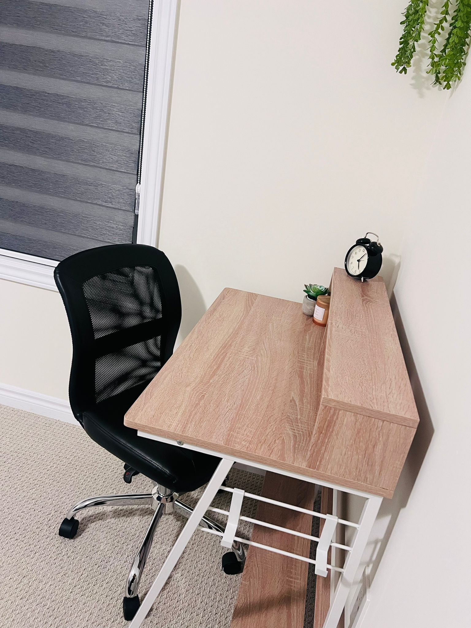 A small, modern office space with a wooden desk, a black mesh office chair, and a small clock on the desk.