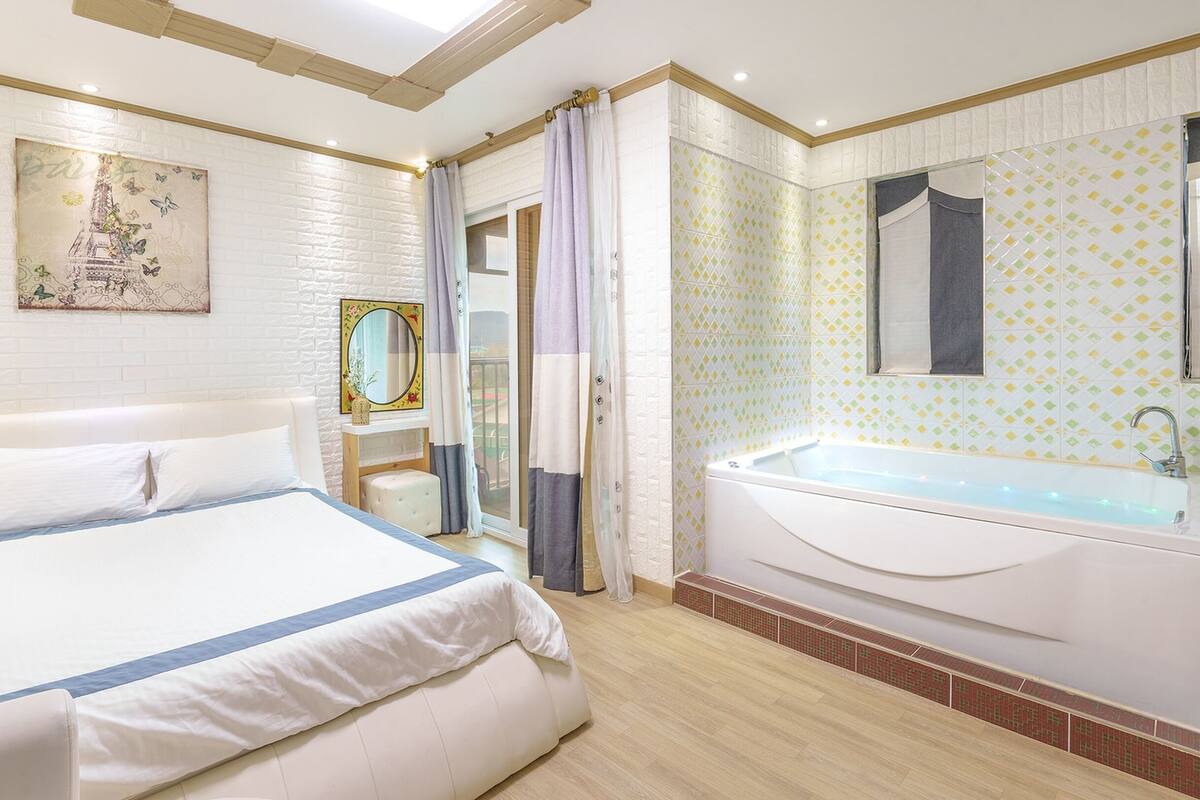 Une chambre d’hôtel avec un grand lit, une baignoire, un miroir et une vue sur l’extérieur.