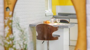 Una cocina con pared de ladrillo blanco, un taburete de madera y una encimera con un vaso y un recipiente pequeño.