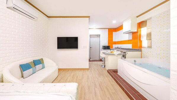 A modern bathroom with a bathtub, a sink, and a toilet. There is a TV mounted on the wall and a window providing natural light. - Gapyeong Nd209 spa Pension (Gapyeong)