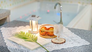 Un coin lecture accueillant avec un livre, un verre d’eau, une bougie et un panier d’oranges posé sur un chemin de table en dentelle.