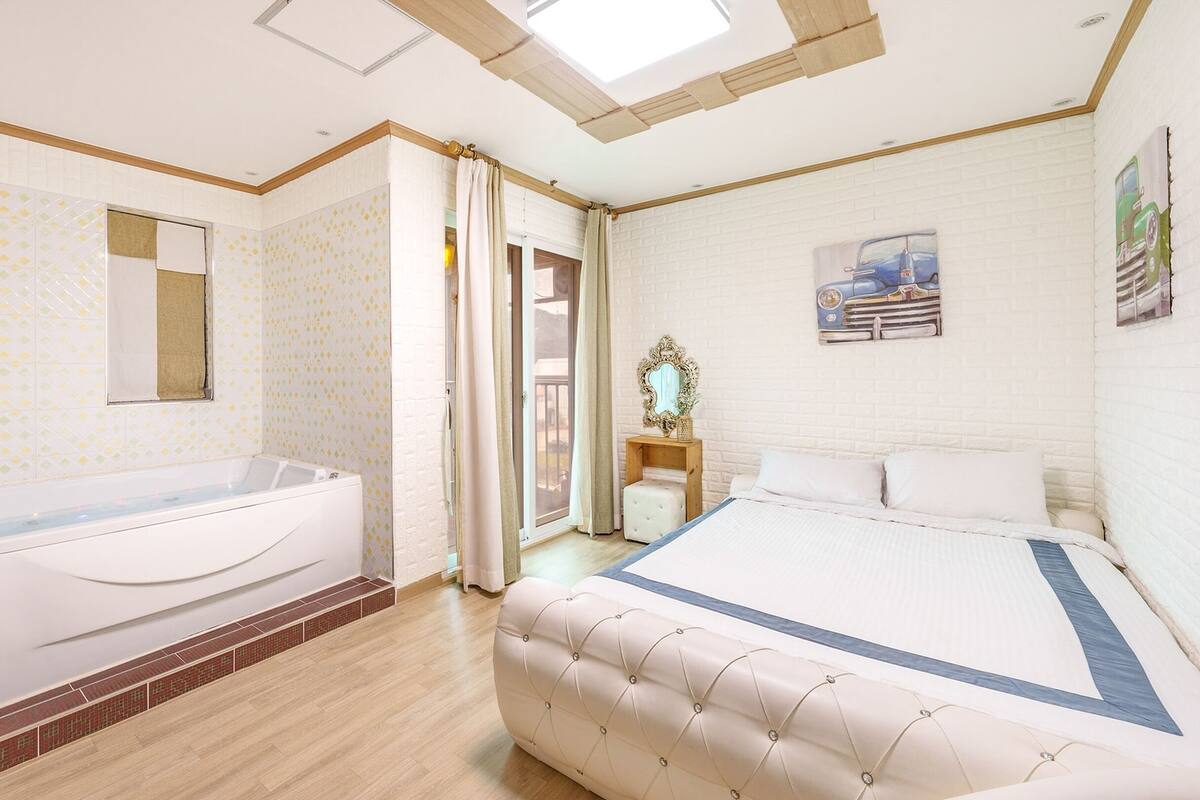 Une chambre avec un grand lit, une salle de bain avec une baignoire et une lucarne.