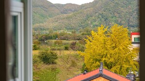 Vista de un paisaje montañoso con un lago, un árbol amarillo en primer plano y un edificio con tejado rojo.