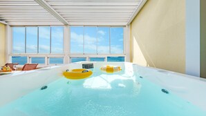 An indoor swimming pool with two inflatable rings, a table with drinks, and a view of the sea through large windows. - Yeosu Stay Raonpine Spa Pension (Yeosu)
