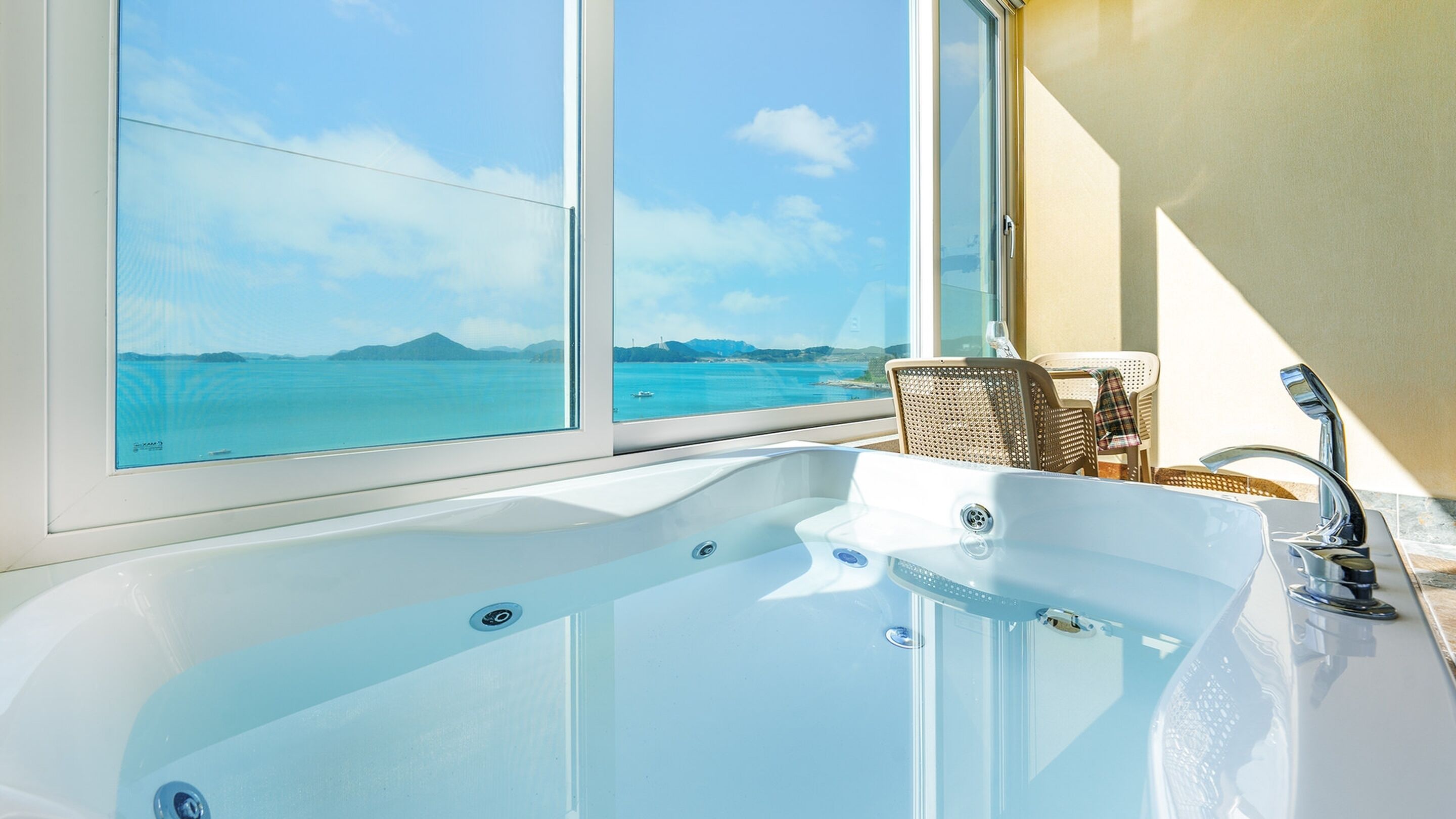 Een badkamer met een groot bad, een raam met uitzicht op zee en een stoel bij het raam.