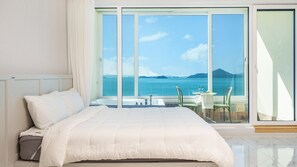 A hotel room with a large bed, a view of the sea, and a balcony with a table and chairs. - Yeosu Stay Raonpine Spa Pension (Yeosu)