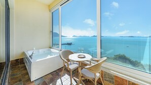 A balcony with a bathtub, wicker chairs, and a table with glasses, overlooking a large body of water and distant islands. - Yeosu Stay Raonpine Spa Pension (Yeosu)