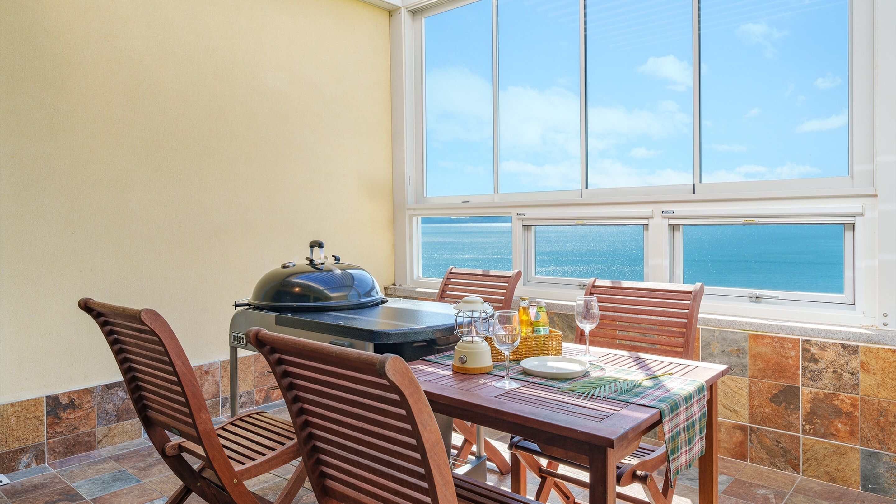 Un balcon avec une table dressée pour les repas, un barbecue et une vue sur la mer.