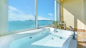 A bathroom with a large bathtub, a view of the sea, and a table with chairs. - Yeosu Stay Raonpine Spa Pension (Yeosu)