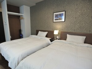 Ein Hotelzimmer mit zwei Betten, einem Nachttisch mit Lampe, einem Kleiderschrank und einer Wand mit Muster.