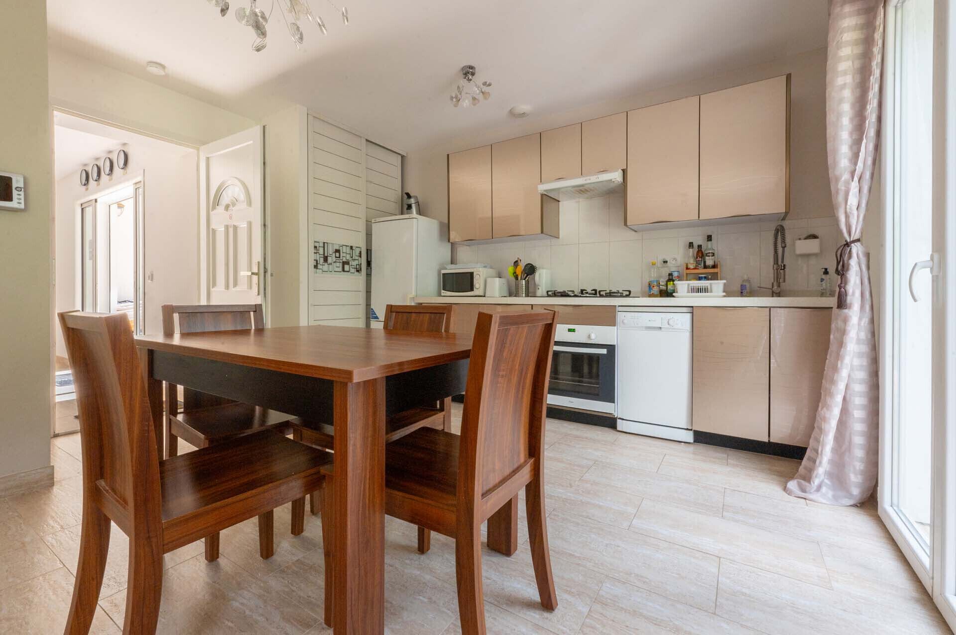 A modern kitchen with wooden cabinets, a dining table with chairs, a microwave, an oven, and a dishwasher.