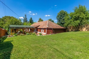Une cabane en bois avec un toit vert, entourée d’une pelouse bien entretenue et d’arbres.