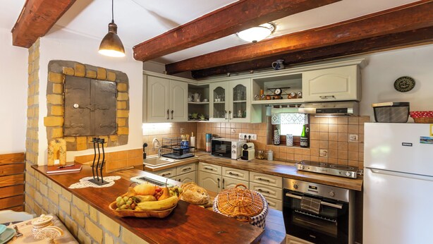 Eine Küche mit Steinwand, Holzbalken und verschiedenen Geräten, darunter Mikrowelle, Toaster und Backofen.