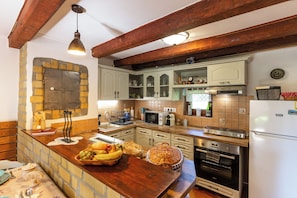 Eine Küche mit Steinwand, Holzbalken, Backofen und weißem Kühlschrank.