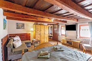 Une chambre avec un plafond en bois, un lit recouvert d’une courtepointe, une armoire en bois, un téléviseur et une fenêtre avec des rideaux.