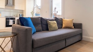 Una sala moderna con un sofá gris, una mesita redonda y una cocina al fondo.
