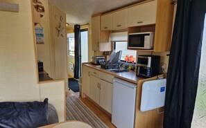 Compact kitchenette with a refrigerator, microwave, toaster, and sink, complete with cabinets and a countertop.