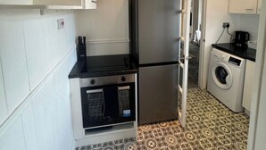 A compact kitchen with a refrigerator, oven, washing machine, and patterned floor tiles. - Simonside Apartment - Sleeps 6 - Pets Ok - Parking (Newcastle upon Tyne)