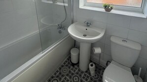 A bathroom with a bathtub, a sink, a toilet, and a window with a plant. - Simonside Apartment - Sleeps 6 - Pets Ok - Parking (Newcastle upon Tyne)