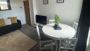 A living room with a sofa, a TV, a round dining table with chairs, and a potted plant. - Simonside Apartment - Sleeps 6 - Pets Ok - Parking (Newcastle upon Tyne)