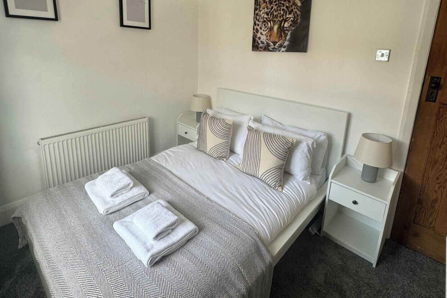 A neatly made bed with a patterned bedspread and pillows, a bedside table with a lamp, and a framed artwork on the wall.