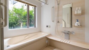 Une salle de bain moderne avec une baignoire, une douche, un grand miroir et une fenêtre donnant sur un paysage verdoyant.