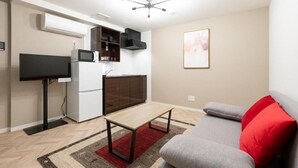 Un espace de vie compact comprenant un coin cuisine, un téléviseur à écran plat, un canapé avec un coussin rouge et un ventilateur de plafond.