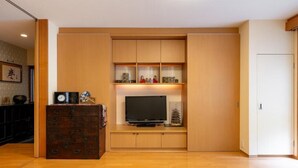 Un salon équipé d’un téléviseur, de meubles en bois et orné d’une œuvre d’art traditionnelle japonaise.