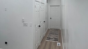 A narrow hallway with white walls, a wooden floor, and a door at the end.