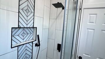 Ein modernes Badezimmer mit Duschkabine aus Glas, weißen Fliesen und einem geometrischen Muster im unteren Bereich.
