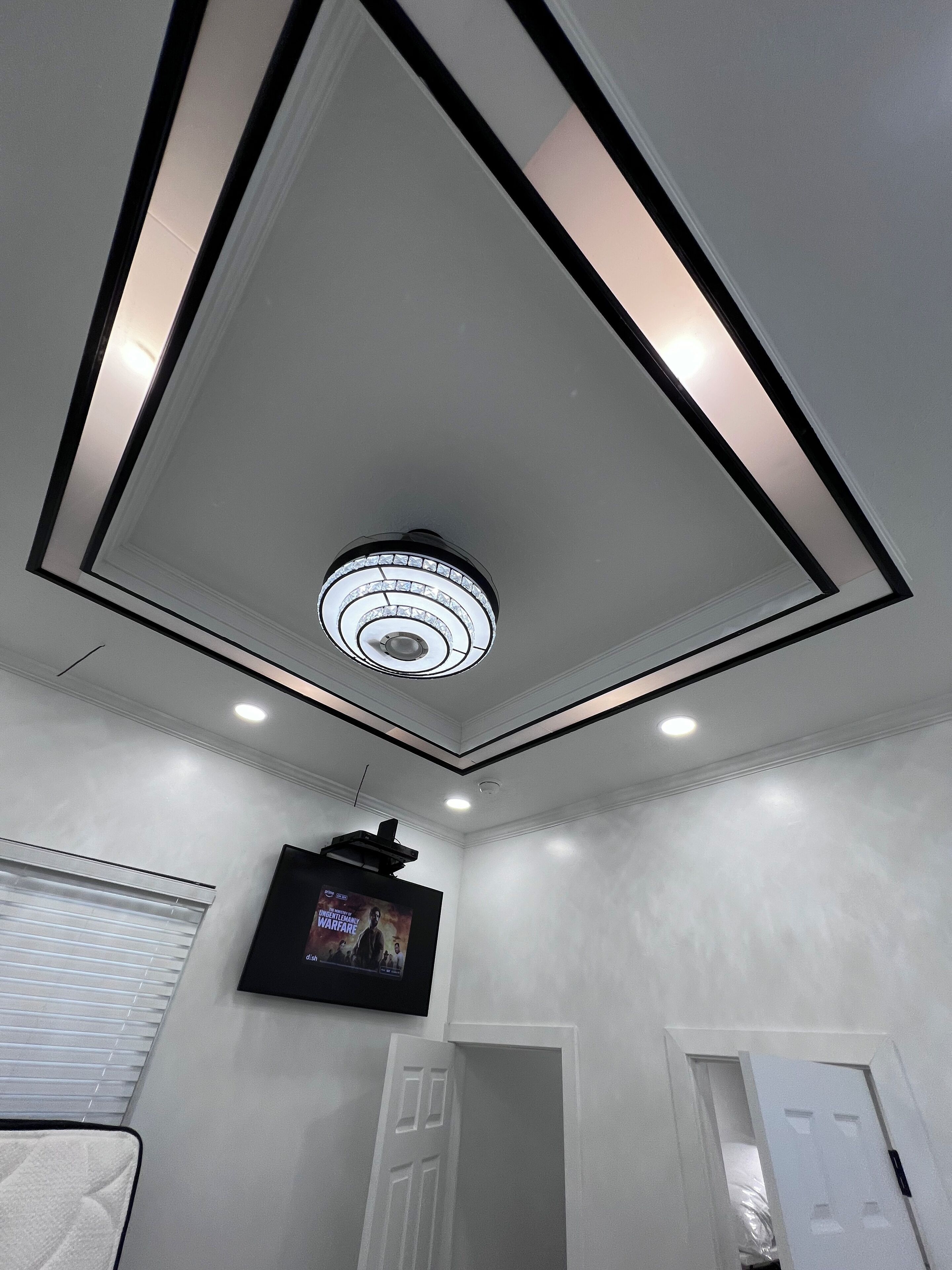 A bathroom with a recessed ceiling light, a wall-mounted TV, and a door leading to another room.