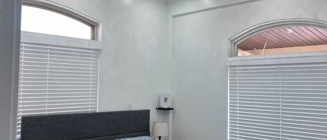 A bedroom with a bed, two bedside tables, a nightstand, a ceiling fan, and a window with blinds.