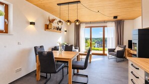 A modern living room with a dining area, a sofa, a TV, and a large window with a view. - Mountain View - Charming townhouse for 4 people with an infrared sauna (Winterberg)