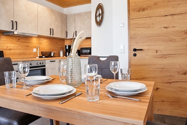 A dining table set with plates, glasses, and cutlery in a modern kitchen with wooden cabinets and a microwave.