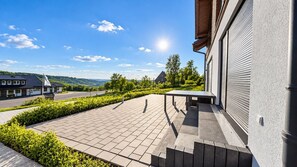 A paved patio area with a table and benches, surrounded by greenery and a view of a road and distant buildings. - Mountain View - Charming townhouse for 4 people with an infrared sauna (Winterberg)
