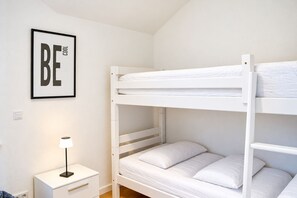 A bunk bed room with a framed motivational poster, a bedside table with a lamp, and a drawer unit.
