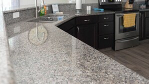 Une cuisine moderne dotée de plans de travail en granit, de meubles de couleur sombre, d’appareils électroménagers en acier inoxydable et d’une poutre en bois au plafond.