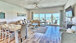 A spacious living room with a dining area, a large window with a view, and a ceiling fan.