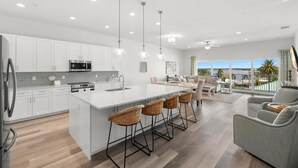 A modern kitchen with white cabinets, a central island with bar stools, stainless steel appliances, and pendant lighting.